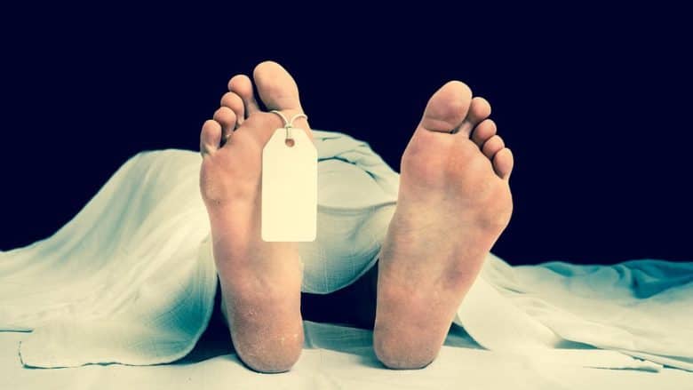 The dead man's body with blank tag on feet under white cloth in a morgue